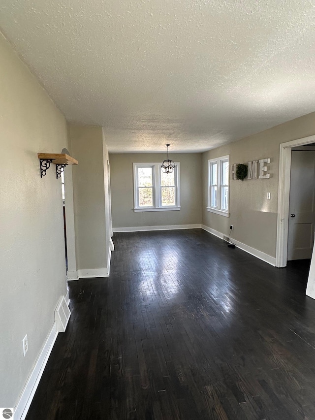 unfurnished dining area featuring dark wood-style floors, baseboards, visible vents, and a textured ceiling