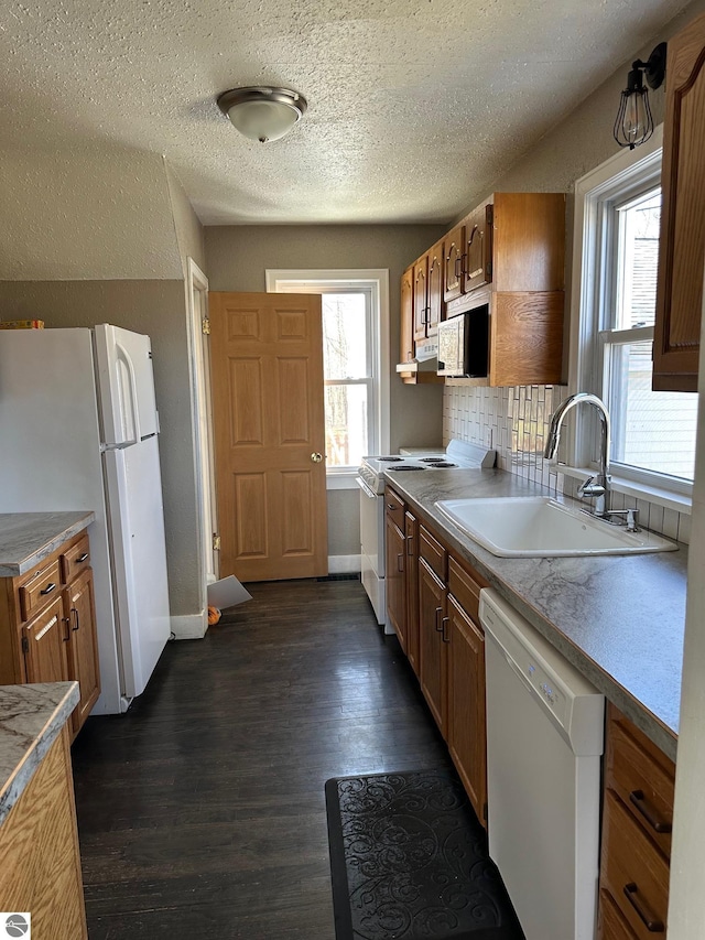 kitchen with dark wood finished floors, white appliances, brown cabinets, a sink, and a textured ceiling