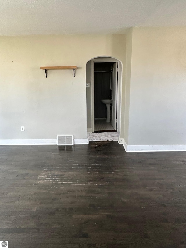 unfurnished room with dark wood finished floors, arched walkways, a sink, baseboards, and visible vents