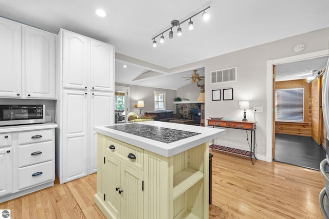 6836 NW Aarwood Trl, Rapid City, MI 49676 - kitchen featuring visible vents, ceiling fan, vaulted ceiling with beams, stainless steel microwave, and light wood finished floors