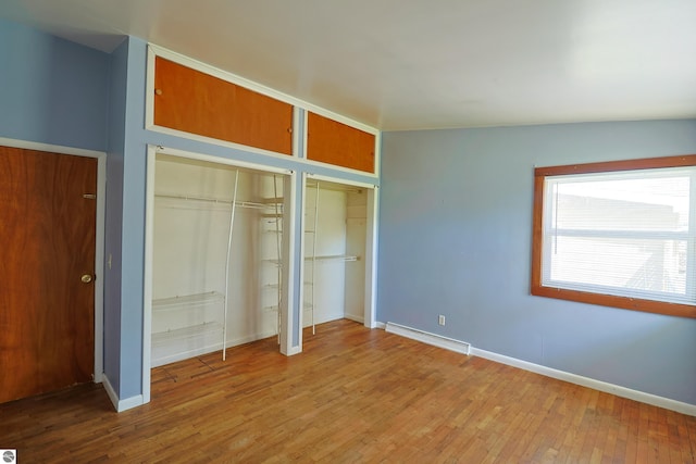 unfurnished bedroom with two closets, baseboards, wood finished floors, and a baseboard radiator