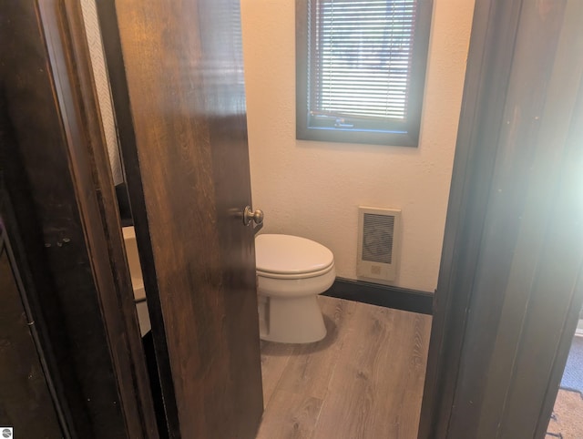 bathroom with baseboards, heating unit, wood finished floors, and toilet