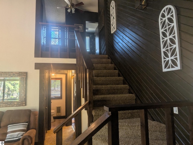stairway with a ceiling fan, wood walls, carpet, and a towering ceiling