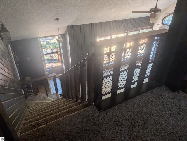 stairs with carpet floors, a textured ceiling, ceiling fan, and wooden walls