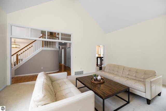 living room featuring visible vents, baseboards, high vaulted ceiling, carpet, and a notable chandelier
