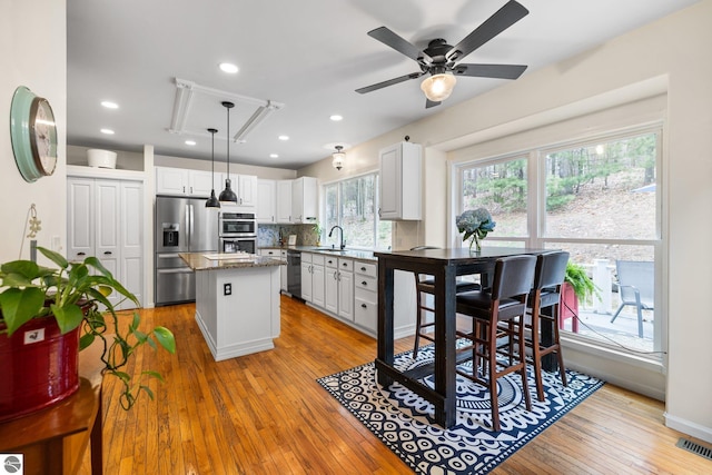 kitchen with a kitchen island, appliances with stainless steel finishes, white cabinetry, a sink, and hardwood / wood-style floors