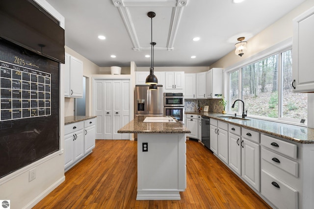 kitchen featuring a kitchen island, appliances with stainless steel finishes, tasteful backsplash, a sink, and white cabinets
