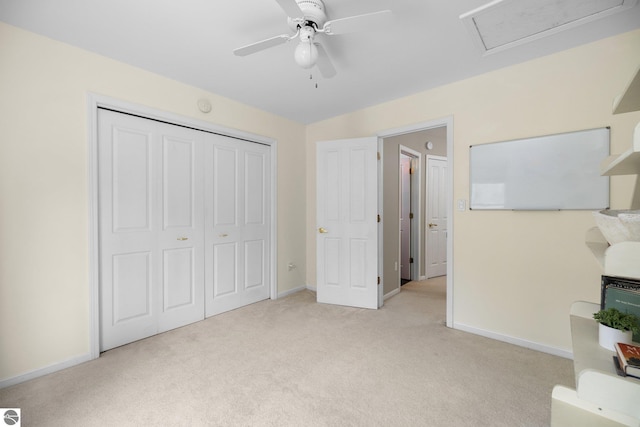 unfurnished bedroom with light carpet, attic access, a ceiling fan, baseboards, and a closet