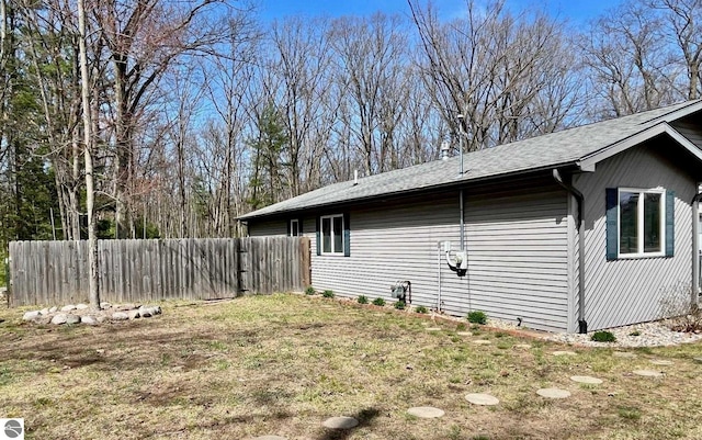 view of home's exterior featuring a yard, fence, and roof with shingles