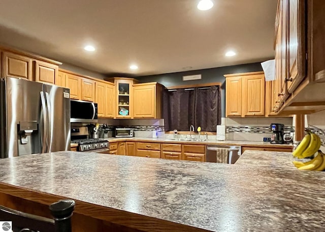 kitchen with appliances with stainless steel finishes, a sink, glass insert cabinets, a breakfast bar, and recessed lighting