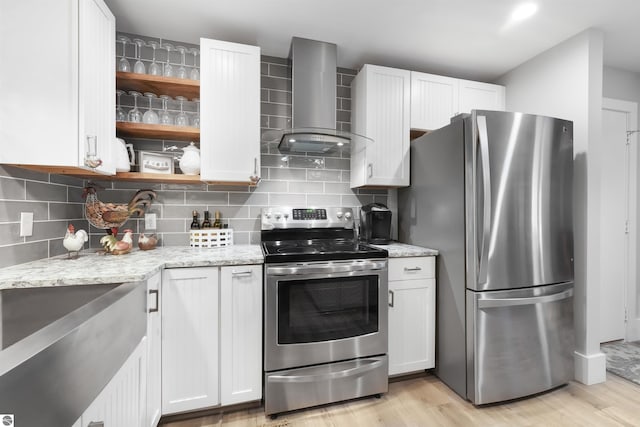 kitchen featuring appliances with stainless steel finishes, light stone counters, wall chimney exhaust hood, and light wood-type flooring