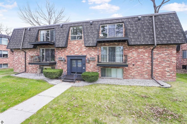 view of front of house featuring brick siding, mansard roof, a balcony, and a front yard