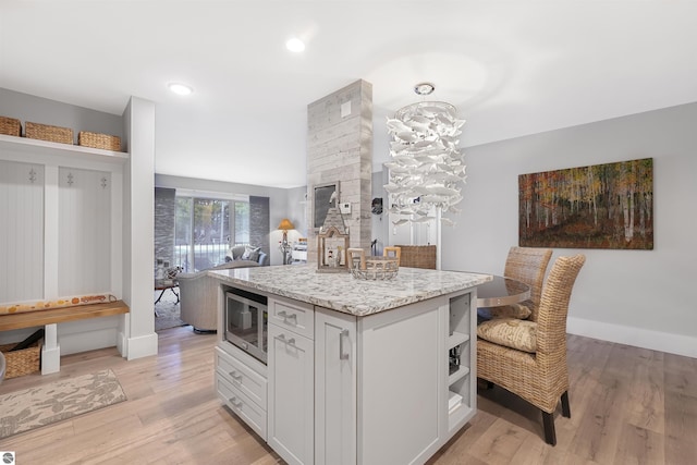 kitchen with light wood-style floors, a center island, stainless steel microwave, and light stone countertops