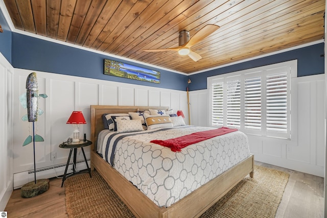 bedroom with a baseboard heating unit, wainscoting, wood ceiling, and a decorative wall