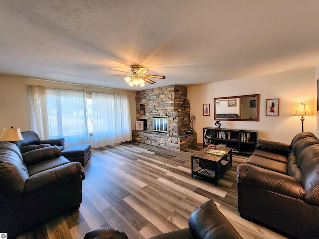 living room with a stone fireplace, a ceiling fan, and wood finished floors