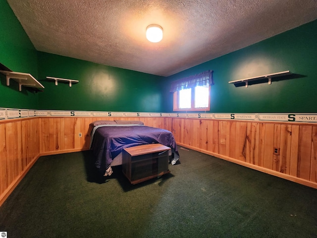 bedroom featuring wooden walls, a textured ceiling, wainscoting, and dark colored carpet