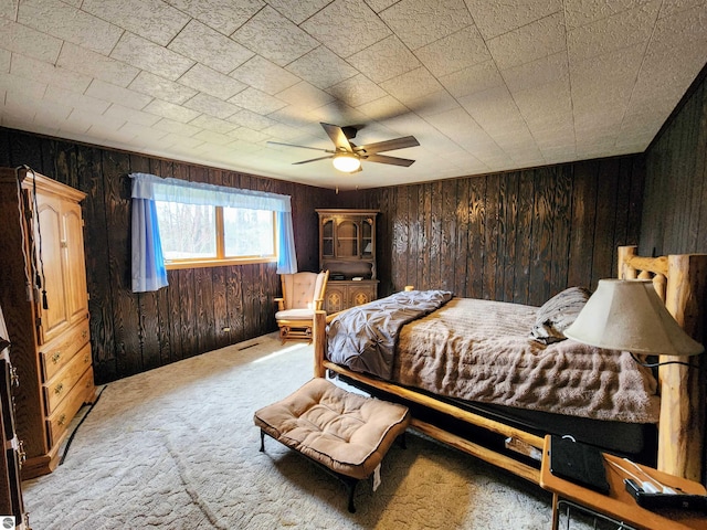 carpeted bedroom featuring a ceiling fan and wooden walls