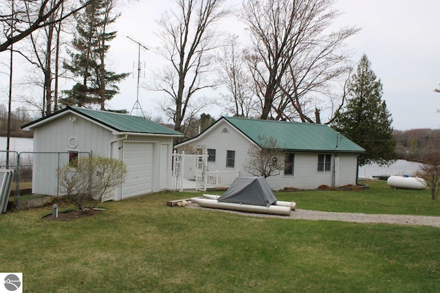 view of front of house featuring metal roof, a front yard, a detached garage, fence, and an outdoor structure