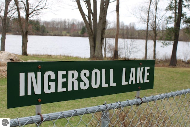 community / neighborhood sign with fence, a water view, and a lawn