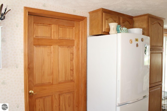 kitchen with freestanding refrigerator, a textured ceiling, and wallpapered walls
