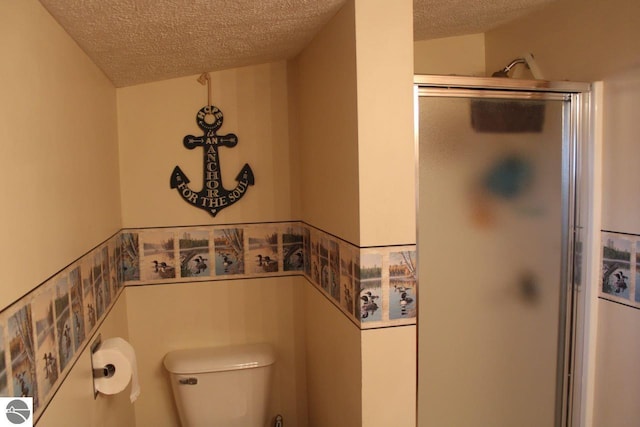 bathroom with a textured ceiling, a stall shower, wainscoting, and toilet