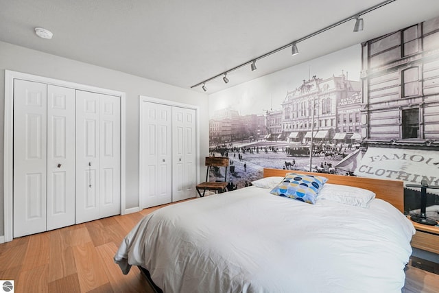 bedroom with two closets, rail lighting, and wood finished floors