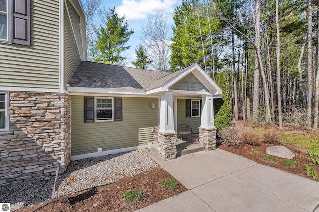 view of front of home with roof with shingles, covered porch, and stone siding