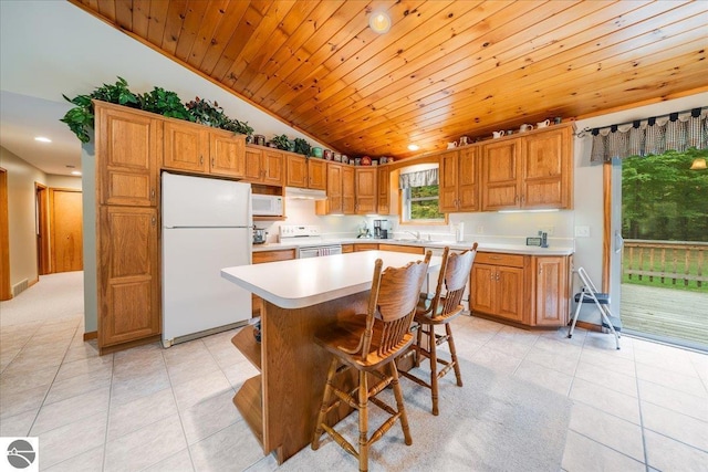 kitchen featuring light tile patterned floors, light countertops, lofted ceiling, under cabinet range hood, and white appliances
