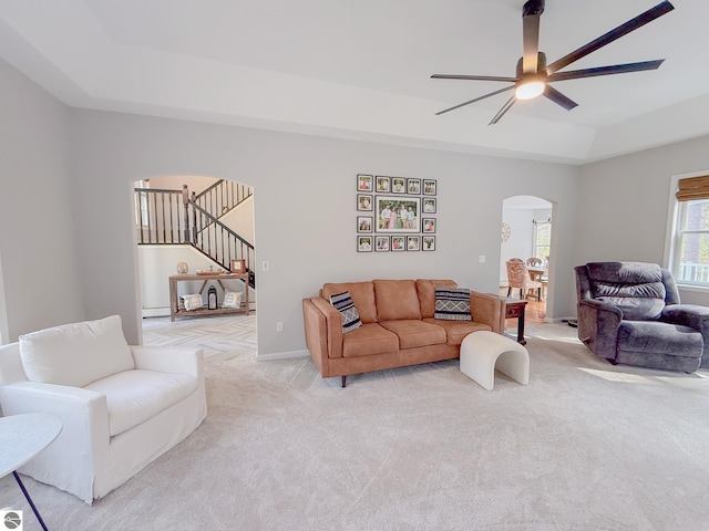 living area featuring a ceiling fan, arched walkways, stairway, light carpet, and a tray ceiling