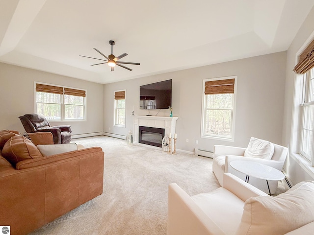 living area featuring a glass covered fireplace, a raised ceiling, a baseboard radiator, and ceiling fan