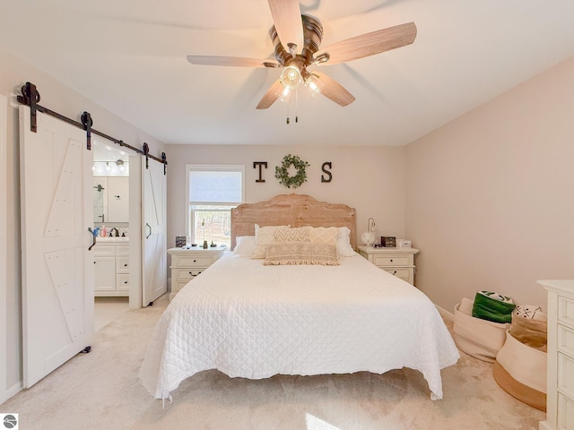 bedroom featuring a ceiling fan, a barn door, a sink, light carpet, and ensuite bath