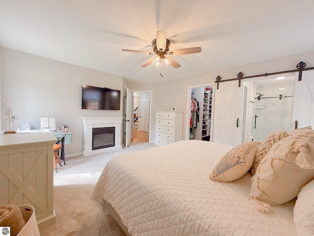 bedroom with ensuite bathroom, light colored carpet, a barn door, and a spacious closet
