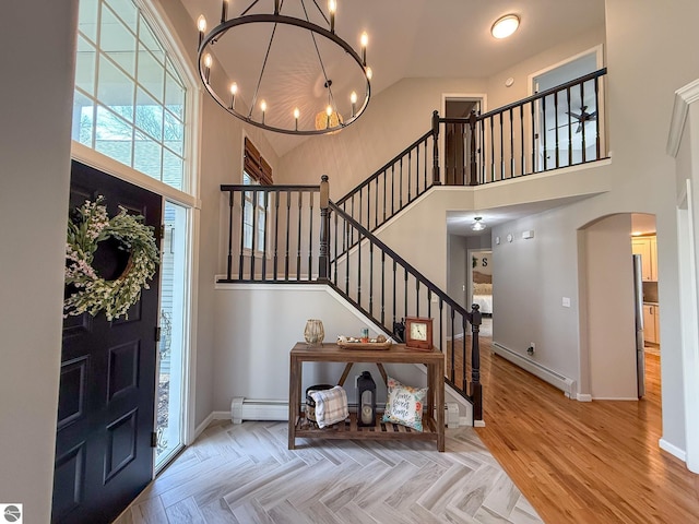 entrance foyer with arched walkways, stairway, a baseboard radiator, a chandelier, and a high ceiling