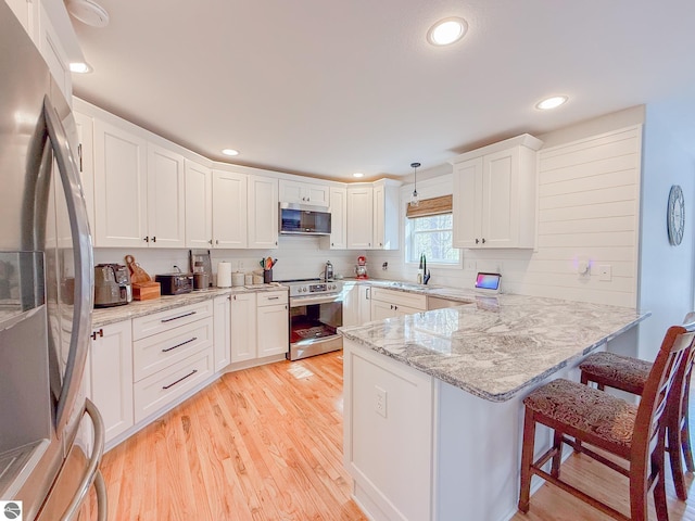 kitchen featuring white cabinets, appliances with stainless steel finishes, a sink, light wood-style floors, and a peninsula