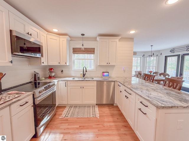 kitchen with a sink, a peninsula, a notable chandelier, light wood-style floors, and stainless steel appliances