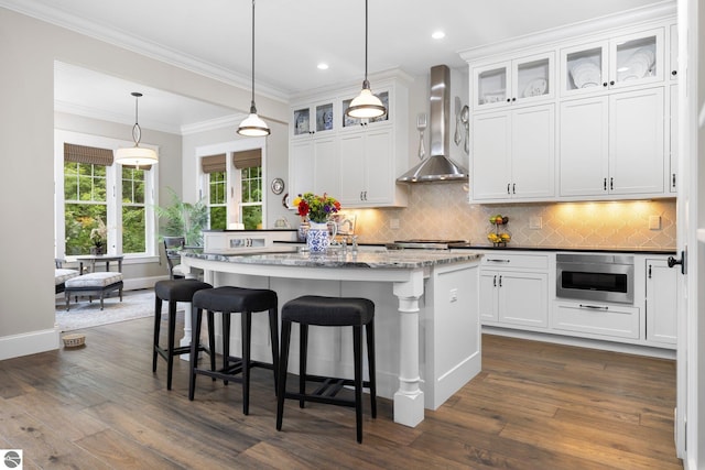 kitchen featuring a breakfast bar area, built in microwave, wall chimney exhaust hood, and dark wood-type flooring