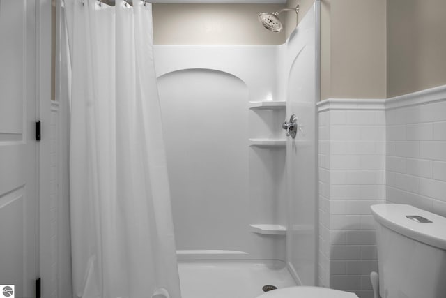bathroom with toilet, tile walls, wainscoting, and a stall shower