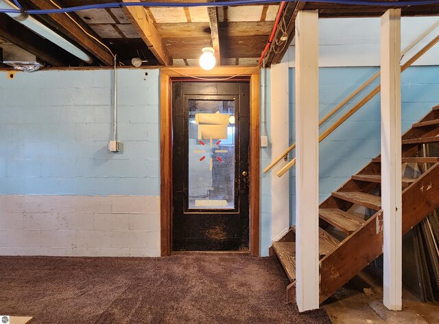 unfinished below grade area with stairway, concrete block wall, and carpet flooring
