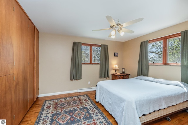 bedroom with light wood-style flooring, a baseboard heating unit, and multiple windows