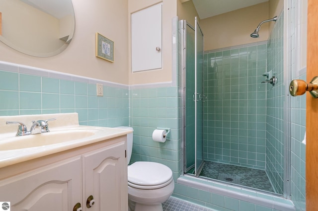 bathroom with tile walls, wainscoting, a stall shower, vanity, and toilet