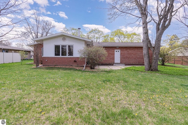 rear view of house with fence, a yard, and brick siding