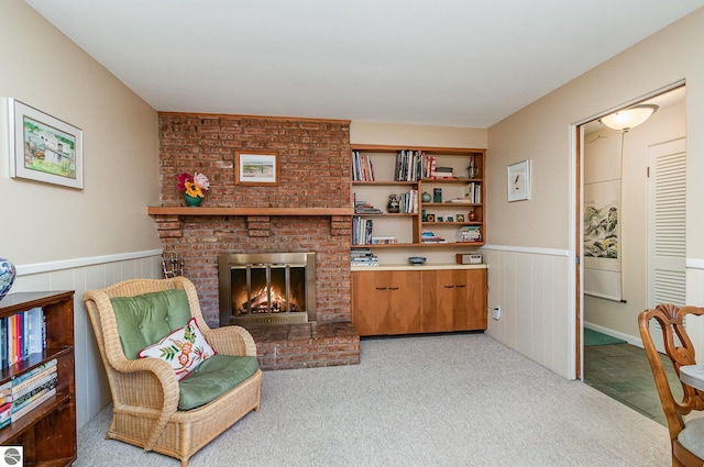 living area featuring a brick fireplace, light carpet, and a wainscoted wall