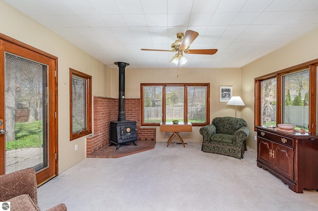 living area with ceiling fan, light colored carpet, and a wood stove