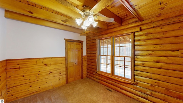 carpeted spare room with ceiling fan, wainscoting, wooden ceiling, beamed ceiling, and rustic walls