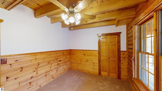 unfurnished room with wood ceiling, a ceiling fan, a wainscoted wall, beamed ceiling, and carpet flooring