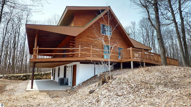 rear view of house featuring log exterior, cooling unit, a wooden deck, and a patio