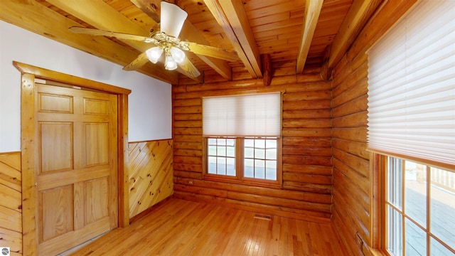 empty room with beamed ceiling, a wainscoted wall, wooden ceiling, a ceiling fan, and light wood finished floors