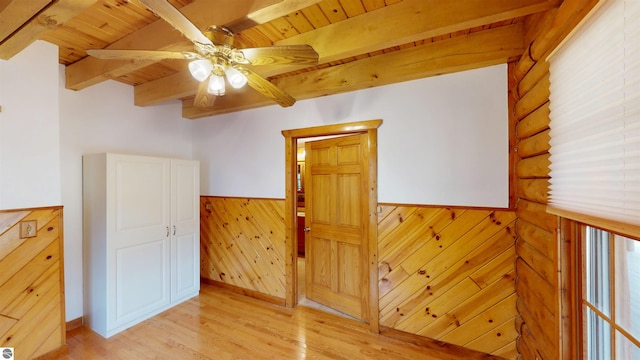unfurnished room featuring beam ceiling, light wood-style flooring, a wainscoted wall, a ceiling fan, and wooden ceiling