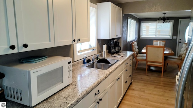 kitchen with a sink, light wood-style floors, white cabinets, and white microwave