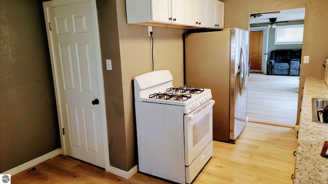 kitchen with baseboards, ceiling fan, white gas stove, light wood-type flooring, and white cabinets